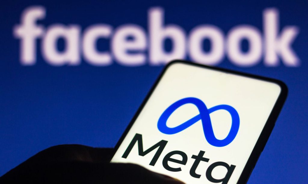  The image shows a hand holding a phone with the Meta logo displayed on the screen with the Facebook logo in the background.